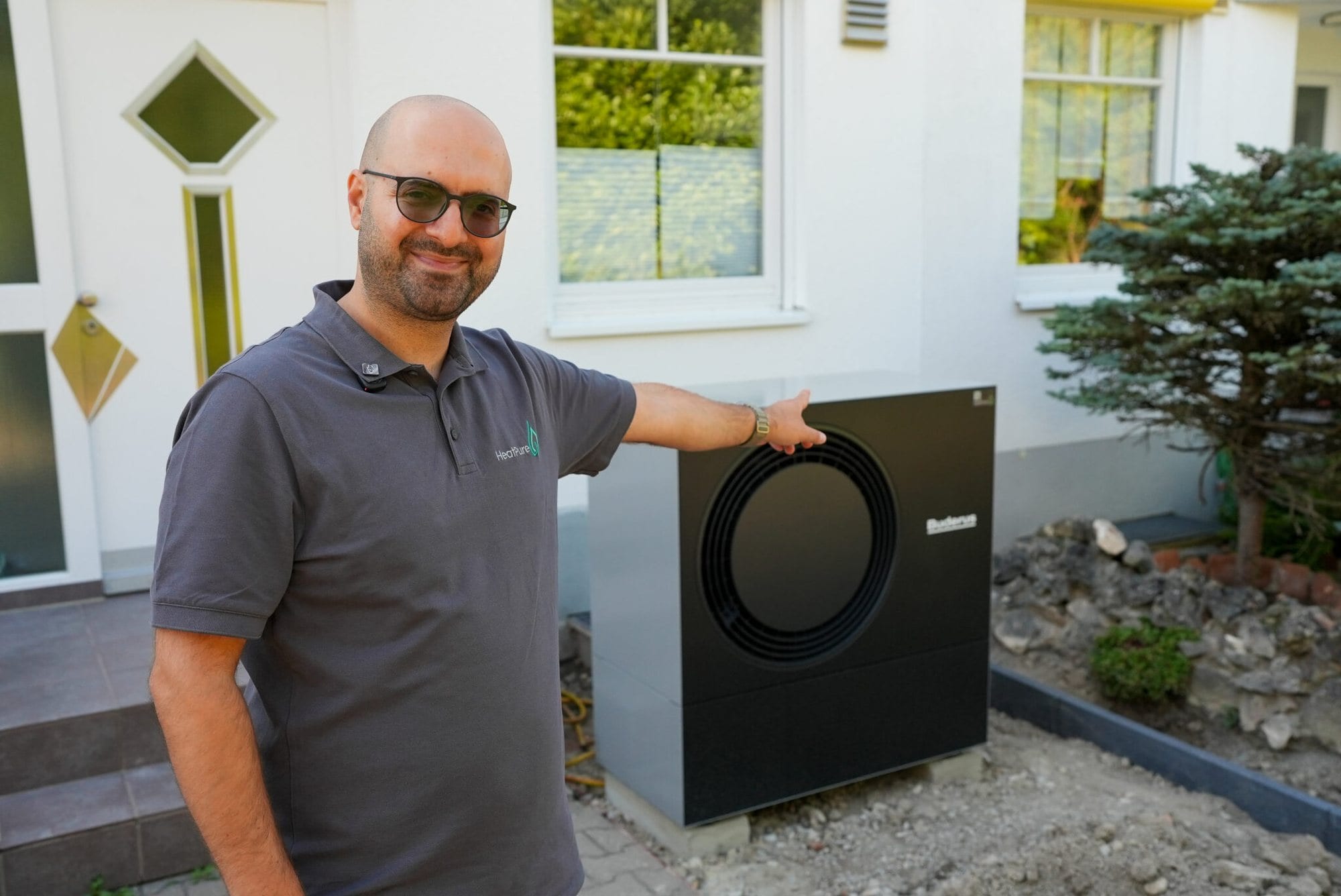 Durmus Pekel von HeatPure neben einer neu installierten Wärmepumpe an einem Wohnhaus im Raum Augsburg